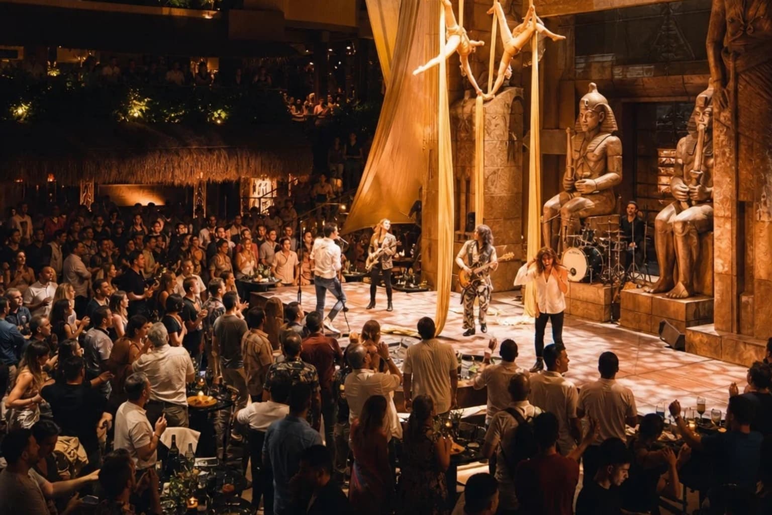 Acróbatas sobre un show egipcio ante el público de Coco Bongo Playa del Carmen, con músicos de rock al fondo