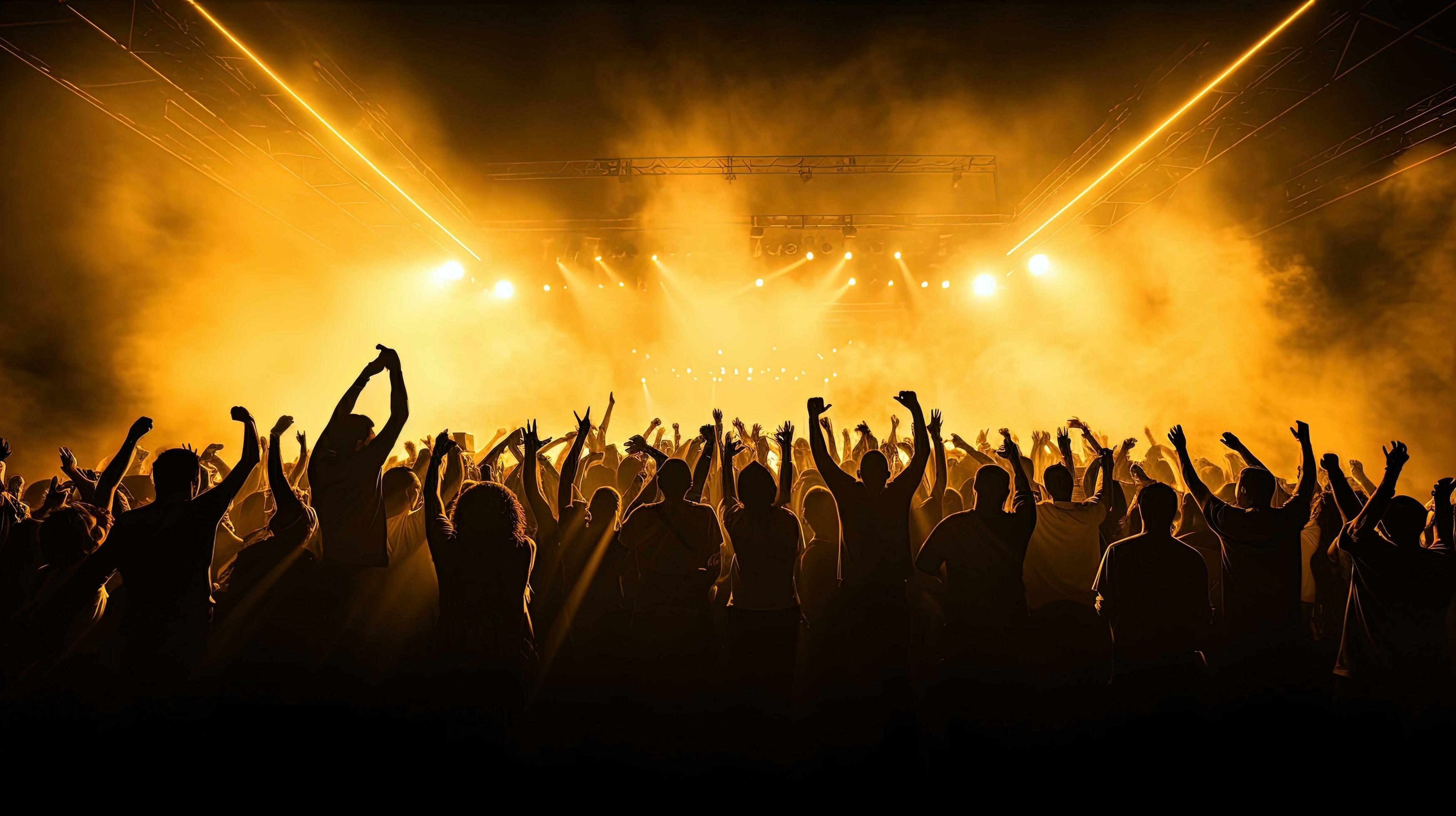 Crowd at a concert with hands raised against golden stage lights